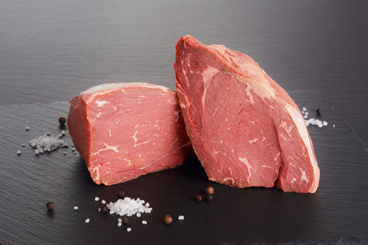 Two raw beef sirloin tip roasts with visible marbling, arranged on a dark slate surface with scattered coarse salt and whole peppercorns.