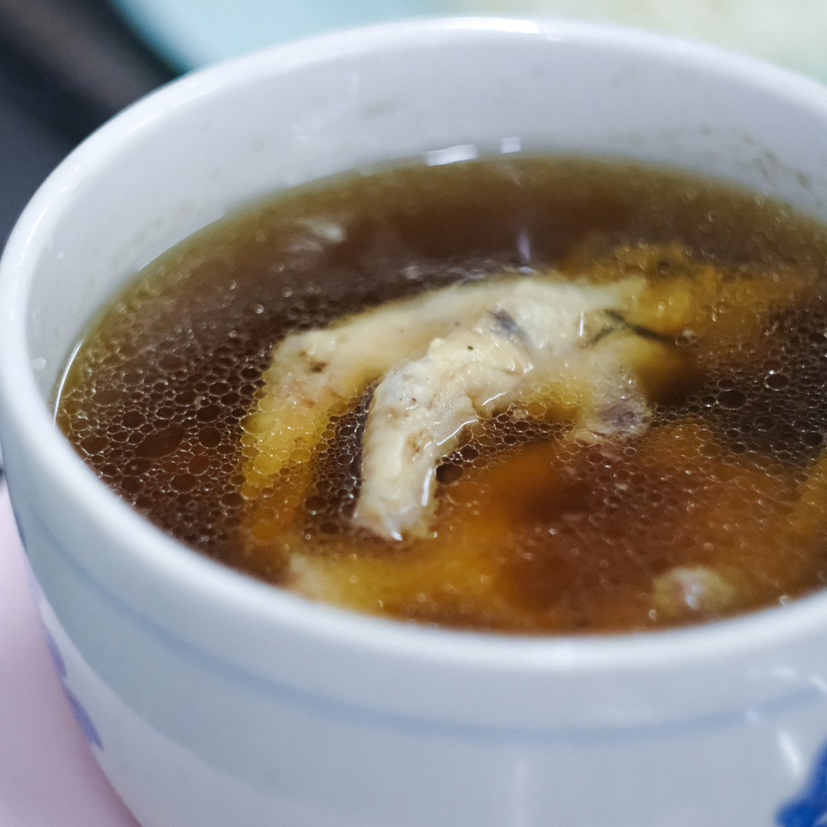 A close-up shot of a white ceramic bowl filled with a hot, bubbling brown soup containing chicken feet.
