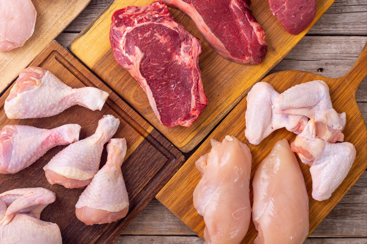 Cuts of grass-fed beef and pastured poultry, raw, displayed on wood cutting boards.