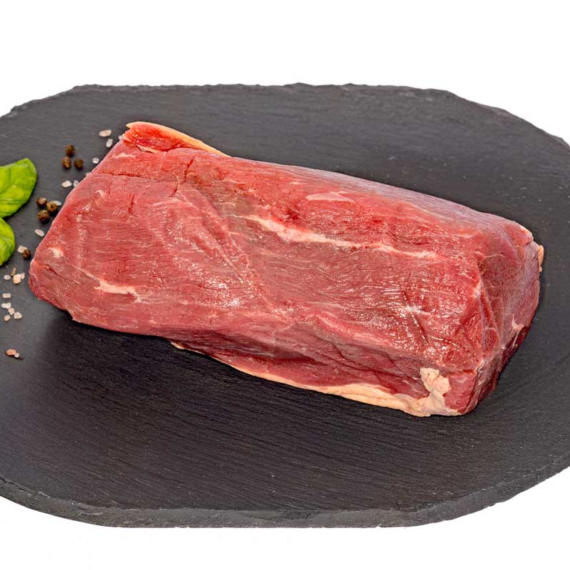A hefty Eye of Round Beef Roast, sitting on a black slate cutting board, next to fresh herbs, pepper, and rock salt.