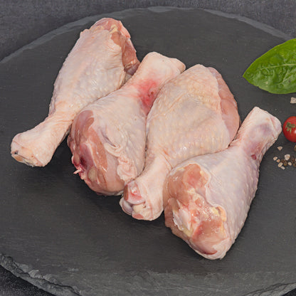 Four raw chicken drumsticks arranged on a dark slate platter with a small green leaf and cherry tomato garnish.
