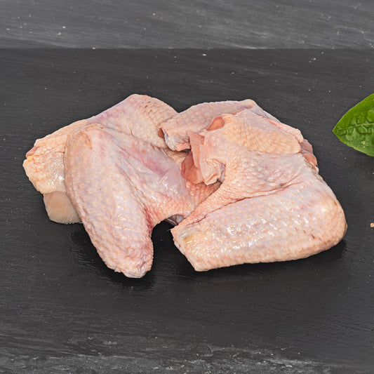 Raw chicken wings and thigh pieces arranged on a dark slate surface with a small green leaf at the edge.